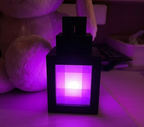 Lámpara farol LED pixel sobre una mesita de noche iluminada en rosa, junto a un peluche