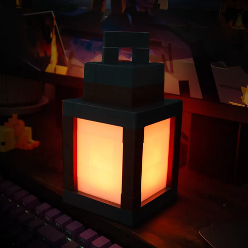 Lámpara farol LED pixel encendida en ámbar cálido sobre un escritorio gamer, junto a un teclado mecánico